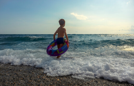 A boy holds an inflatable ring and admires waves at the beach