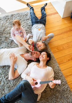A mother and father play a ukulele with their son and baby indoors