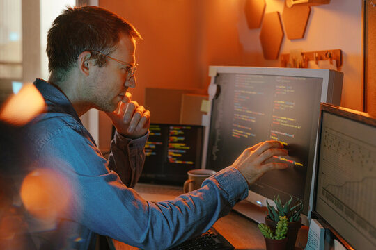 Businessman pointing at computer screen while analyzing code at night