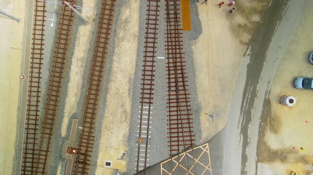 Top down view of parallel railway tracks beside a maintenance crew and parked vehicles at a train depot