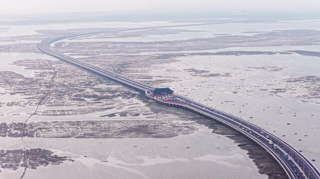 Overwater highway bridge and toll plaza gate with traffic passing through on an elevated causeway crossing exposed coastal mudflats at low tide aerial drone view in Bali Indonesia