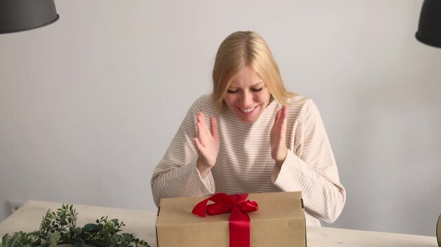 Overjoyed woman claps and cups her cheeks in happy disbelief while receiving a wrapped Christmas gift box with a red ribbon bow, a joyful New Year present and festive holiday surprise idea for women