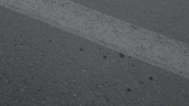 A slow downward pan reveals the textured, cracked surface of a weathered asphalt road, where a faded white line exits the frame to expose small debris and wear.