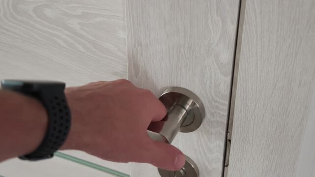 Close up shows a hand turning a metal lever handle and opening a light wood interior door, revealing a darker room beyond