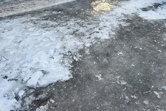 Thin layer of snow and ice covering a dark asphalt road background during a cold winter day