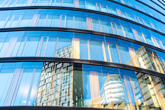 Curved glass facade with blue windows and reflections of buildings creates modern urban architecture as the windows follow the facade and hold reflections of buildings