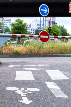 Bicycle lane marking on an urban road leads toward traffic signs and a barrier where street mobility is directed by the traffic signs and road marking
