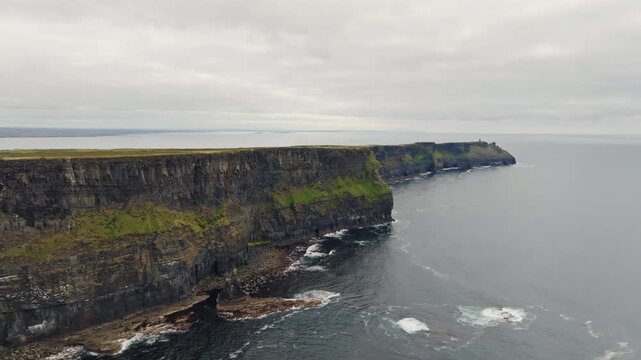 Cliffs of Moher in County Clare, Ireland. An aerial panorama follows sea cliffs and the Atlantic Ocean under overcast weather, a coastal destination for sightseeing.