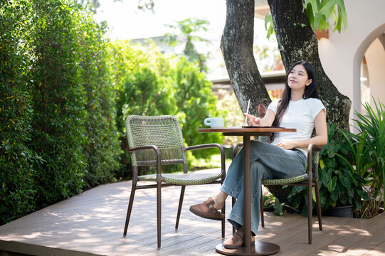 Asian Woman Relaxing on Chair with Digital Tablet in Garden