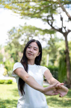 Asian Woman Stretching Arms and Warming Up Outdoors in Park