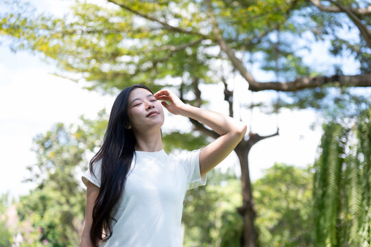Asian Woman Touching Hair Enjoying Warm Sunlight Outdoors in Park
