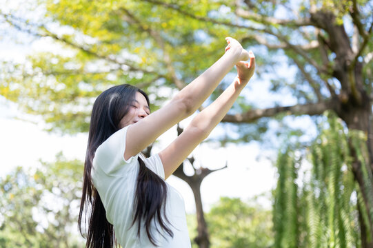 Asian Woman Stretching Arms Upward Towards Sky Outdoors in Park