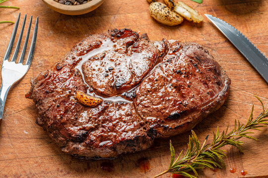 Grilled ribeye steak (entrecote) on wooden board with garlic, rosemary and spices.