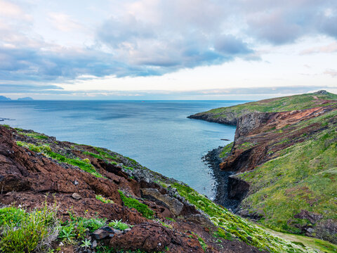 A high-angle view of the deep blue sea meeting a distant flat rocky island from the slopes of Ponta de Sao Lourenco, Madeira, Portugal.