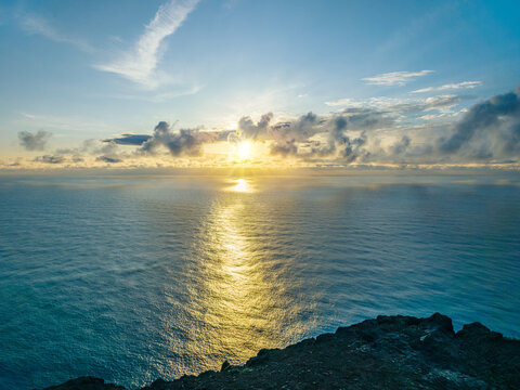 Breathtaking golden sunset over the calm Atlantic ocean with sun rays breaking through clouds at Ponta do Pargo, Madeira, Portugal.