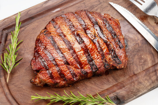 Grilled beef ribeye steak with rosemary on wooden cutting board.