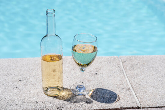 Glass and open bottle of white wine on concrete pool edge
