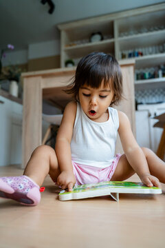 Toddler white girl reading book on floor at home in Spain