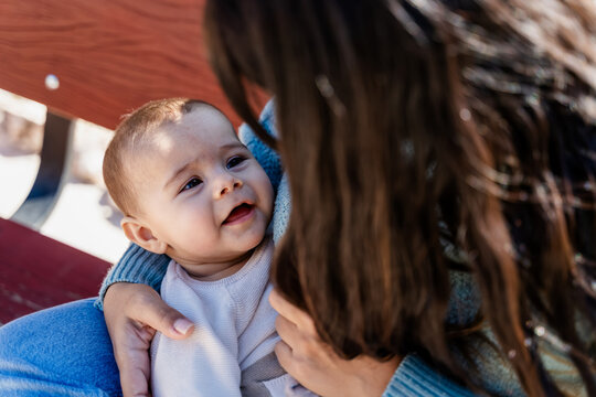 Baby smiling in white woman's arms on outdoor bench