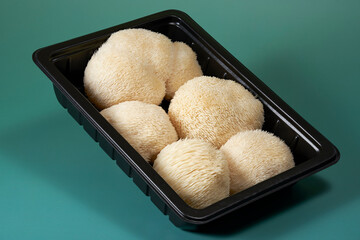 Fresh Lion’s Mane mushrooms (Hericium erinaceus) arranged in a black food tray against a green background, highlighting distinctive spiny texture for culinary and functional food concepts. © DEWINs