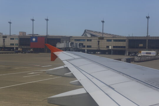 View of airplane wing looking toward airport terminal with Taiwan flag.