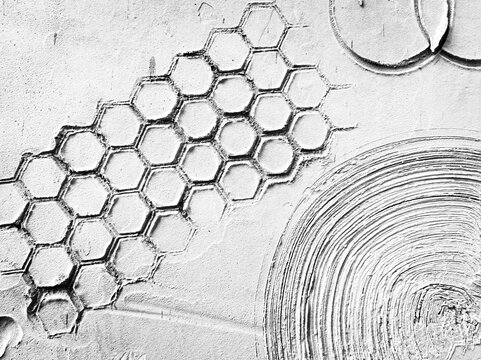 Abstract white plaster wall texture featuring hexagonal honeycomb patterns and circular geometric relief art.