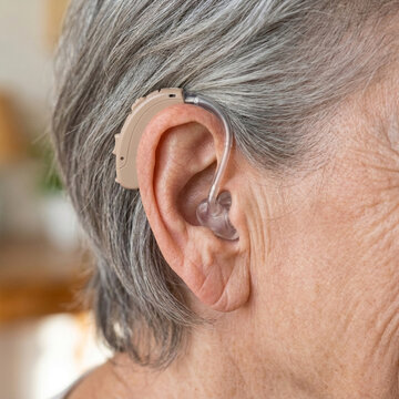 Close up of senior womans ear with modern beige hearing aid device improving hearing and communication