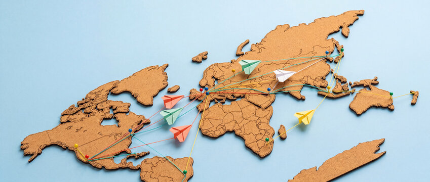 World map with flight routes and paper airplanes marked by colorful pins and strings on cork board over blue background, perfect for travel agency, tourism, and vacation planning