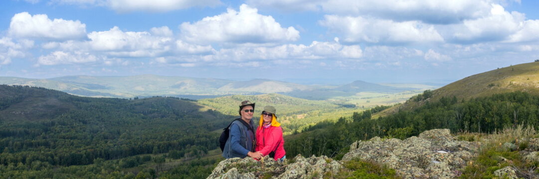 Tourists sit on a rocky outcrop, gazing into the distance at the Irendyk Ridge in the Southern Urals on a misty morning.