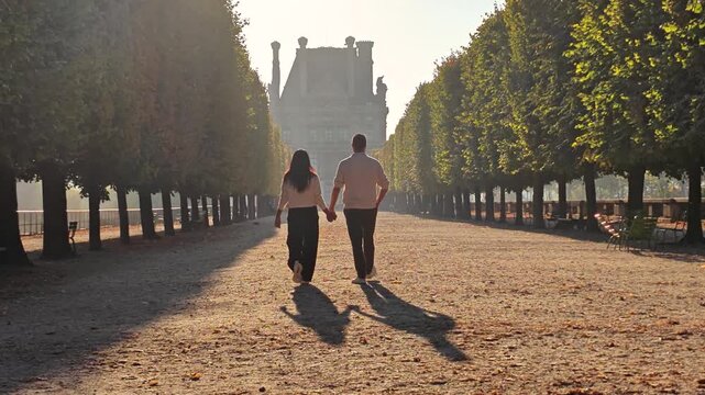 A couple walks hand in hand through the serene path of Tuileries Garden in Paris, France, surrounded by beautiful trees and breathtaking morning light.