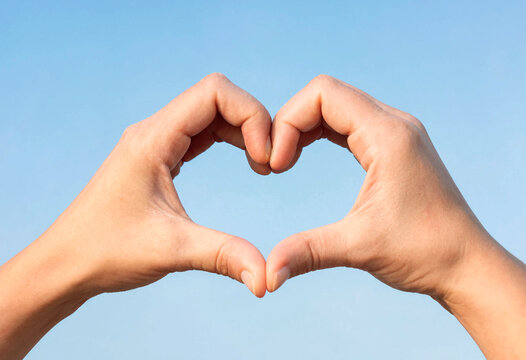 Two hands forming heart shape against clear sky background
