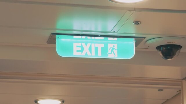 Illuminated Green Exit Sign and Security Dome Camera on Building Ceiling