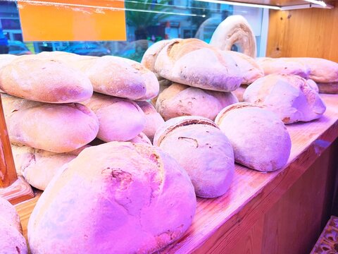 View of a traditional bakery display case showing a variety of rustic breads, loaves, baguettes, and freshly baked homemade empanadas with small descriptive chalkboard signs.