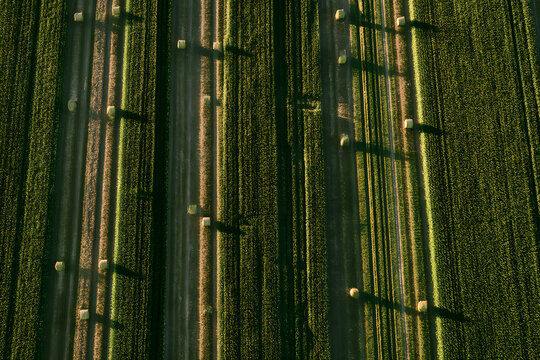A top-down aerial view of wheat and corn fields at sunset, highlighting parallel lines and haystacks; a scene that evokes the agricultural landscape of Normandy, a mix of green and gold