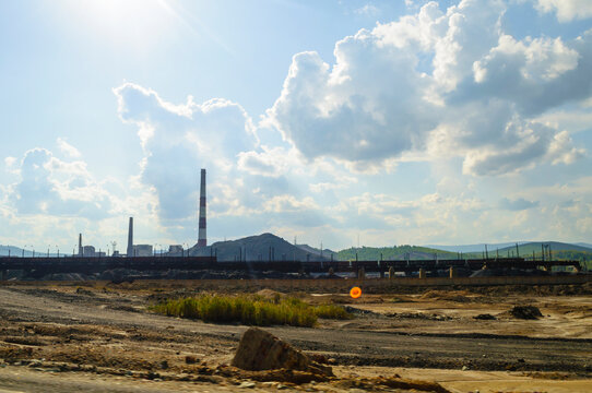 Industrial landscape background with a large dark slag heap and smokestacks at a factory under a bright blue sky with white clouds