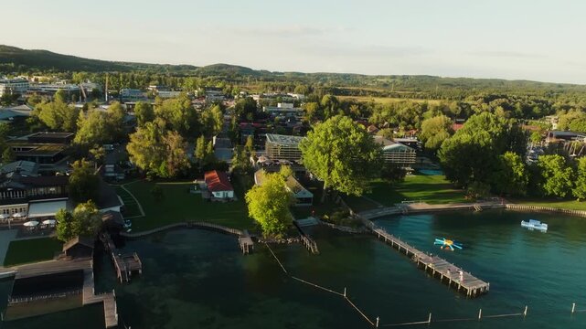 A drone flies backward over Lake Starnberg in Germany, moving farther from the tree-lined shore and revealing a wider view of piers, lakeside buildings and boats.