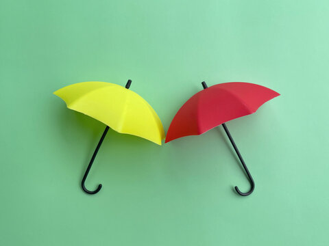 Yellow and red umbrellas arranged side by side against a mint green background, creating a colorful minimalist concept for protection and rainy weather.