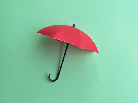 Red umbrella isolated against a mint green background, featuring a clean minimalist composition symbolizing rain protection, weather and outdoor lifestyle.