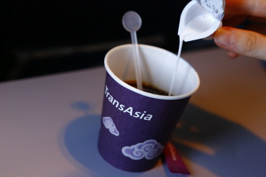 Pouring coffee creamer into inflight hot coffee cup on tray table.