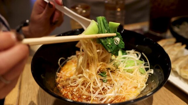 Person Lifting Noodles with Chopsticks from Spicy Ramen Bowl