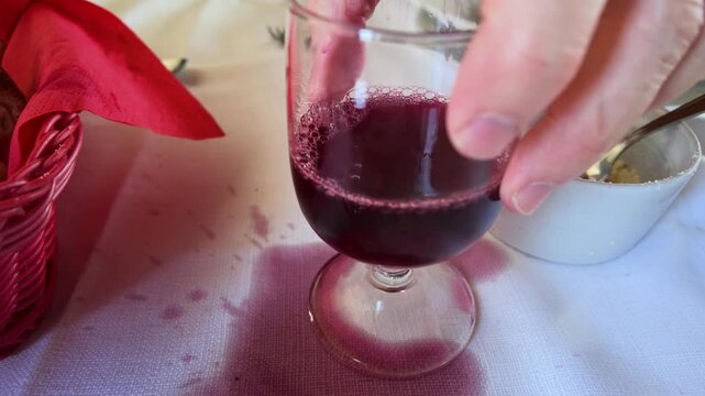 Person Lifting Wine Glass from Spilled Red Wine on Restaurant Tablecloth