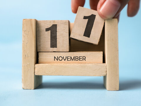 A woman's hand is holding a wooden block with the number 1 written on it on a wooden block calendar for November 11th on a light blue background.