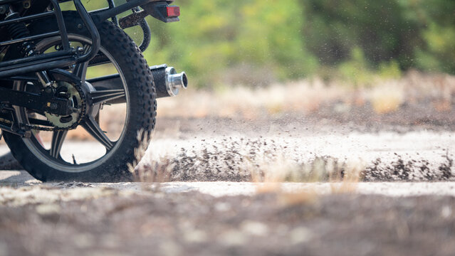 Motorcycle wheel kicking up dust on a dirt road in a forest during daytime