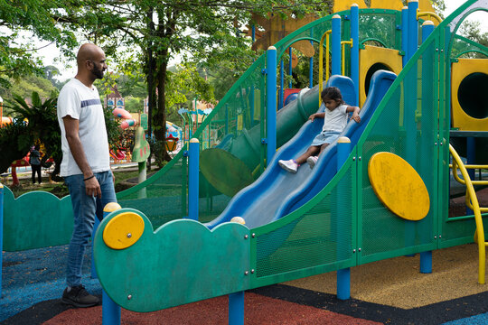 Father watching daughter sliding down playground slide
