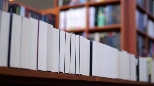 White bound books stand in neat row on wooden library shelves. Quiet collection of blank spines sits before softly blurred bookshelves, suggesting organized study and research, aligned along wooden