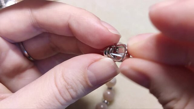 Detailed assembly of natural sunstone gemstone beads threaded with silver components and metallic hardware on a neutral workspace surface