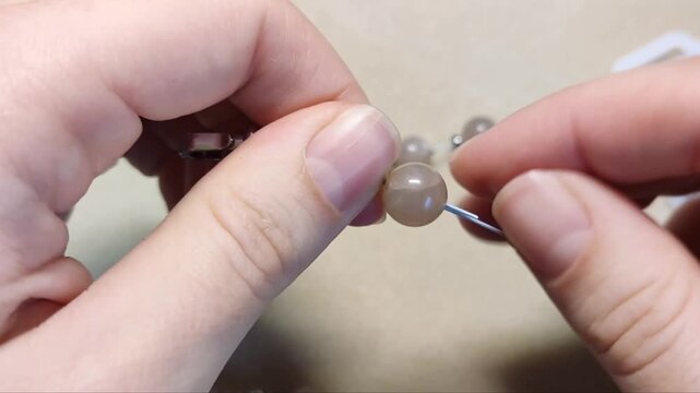 Detailed assembly of natural sunstone gemstone beads threaded with silver components and metallic hardware on a neutral workspace surface