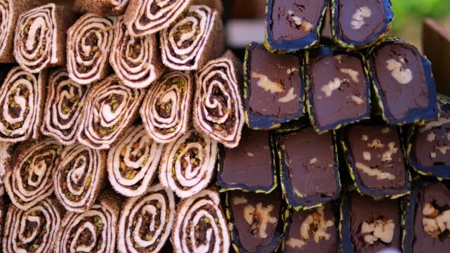 Assorted artisan sweets fill display with chocolate coated bars and spiral pastries. Decorative confections show layered patterns and nut pieces, offering rich selection of handcrafted treats.
