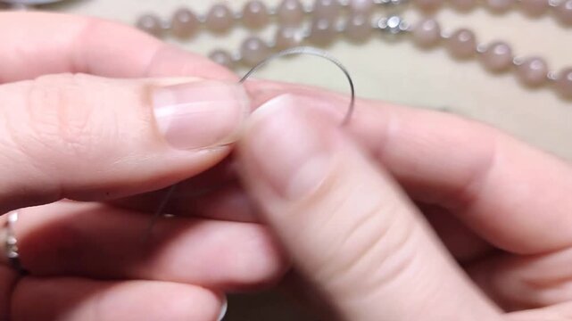 Detailed technique of threading smooth natural sunstone gemstone beads onto flexible wire alongside polished silver elements and finished necklace layouts on a clean neutral surface