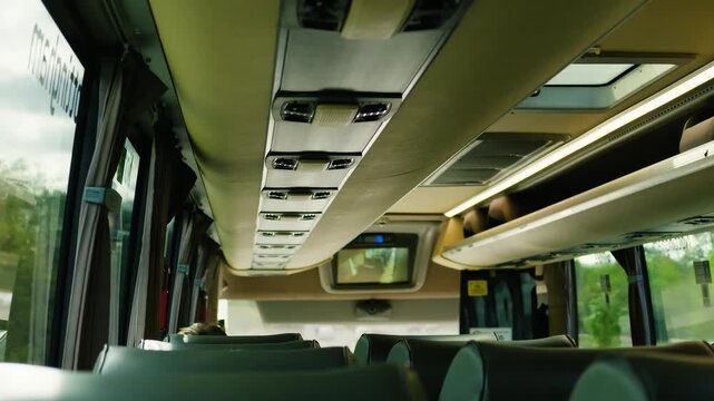 Modern intercity bus interior with passenger seats and overhead luggage racks. Coach cabin ceiling with air vents, reading lights and skylight. Long distance public transport interior during daytime